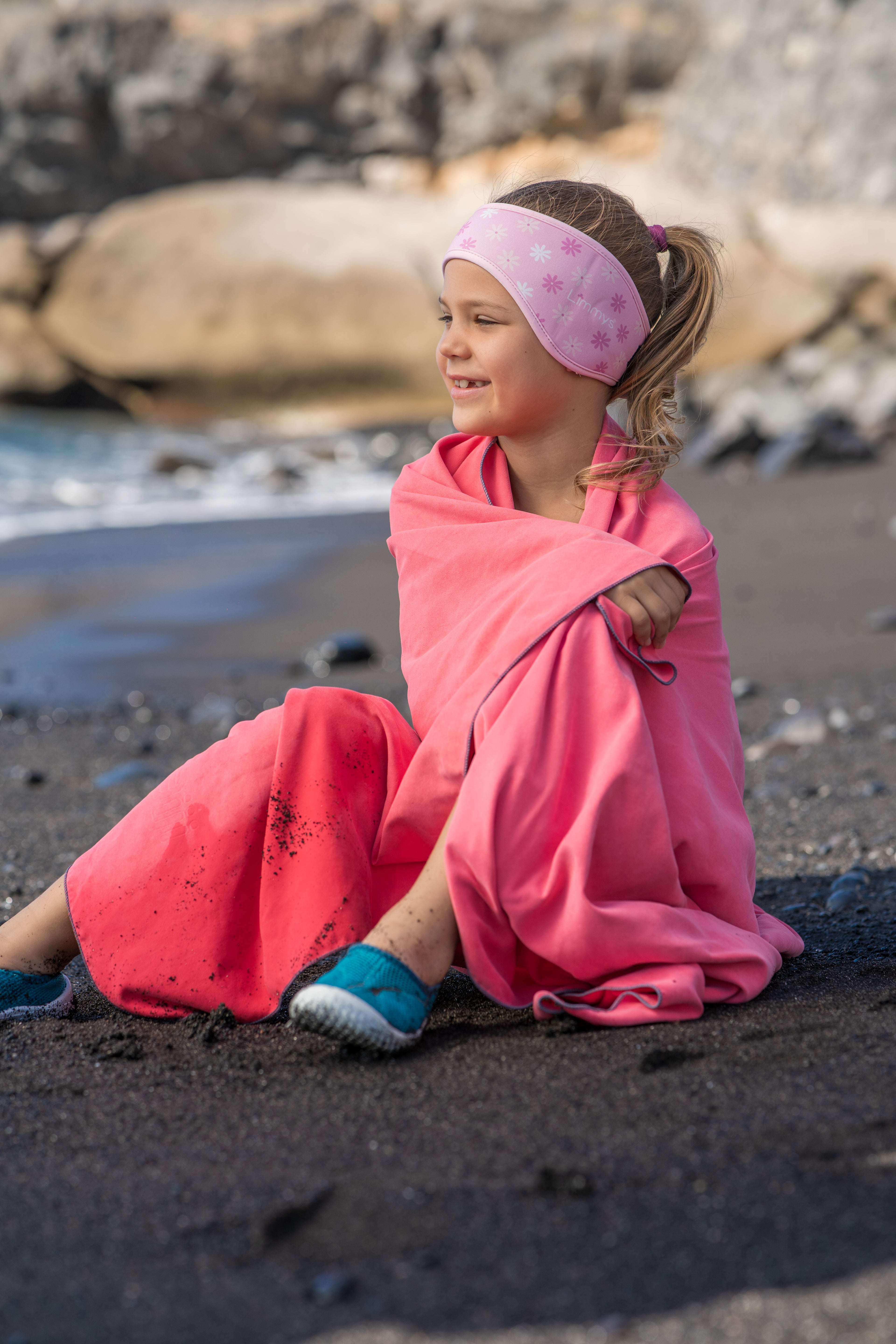 Child on the beach after a swim in the ocean wearing her pink flower ear-protecting headband.