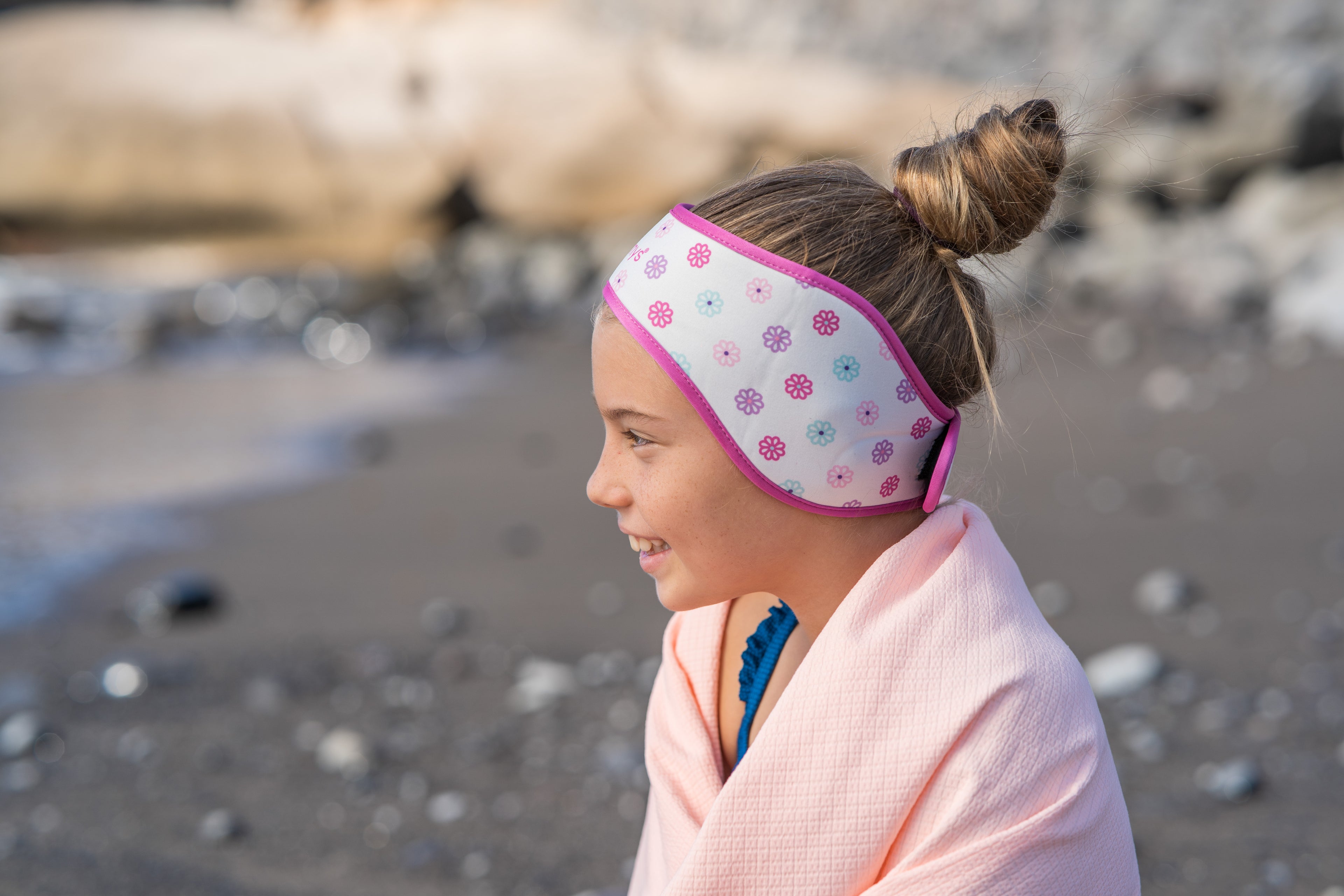 Girl on a beach wearing a pink flower headband with colorful patterns.