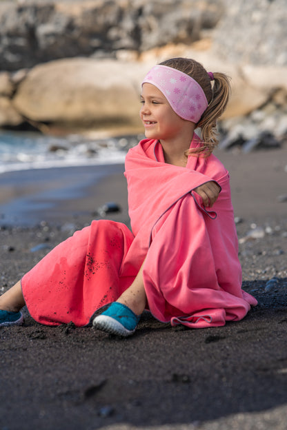 Child on the beach after a swim in the ocean wearing her pink flower ear-protecting headband. 